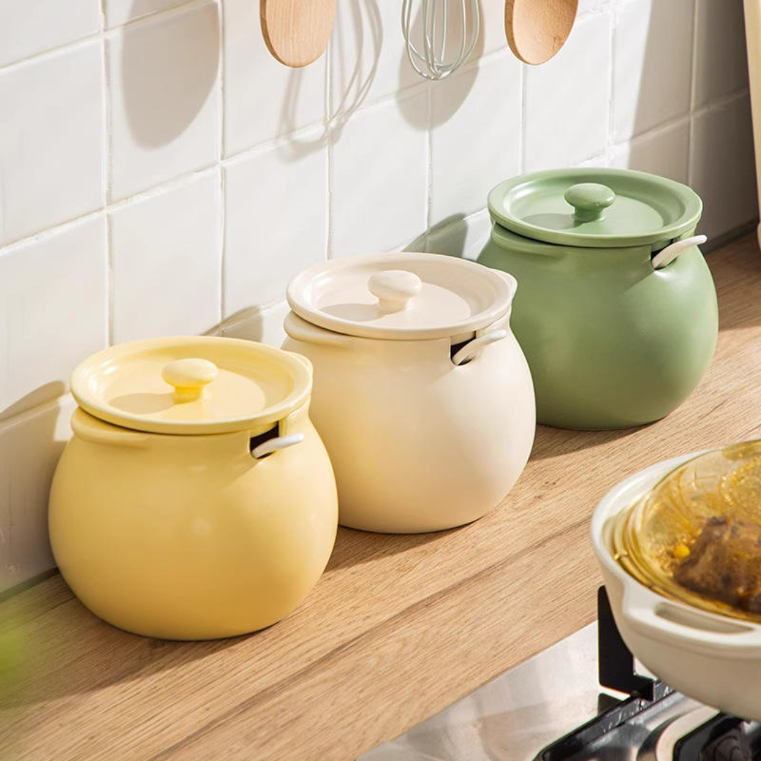 Three ceramic canisters with lids in yellow, cream, and sage green, arranged on a wooden kitchen countertop against a white tiled wall.