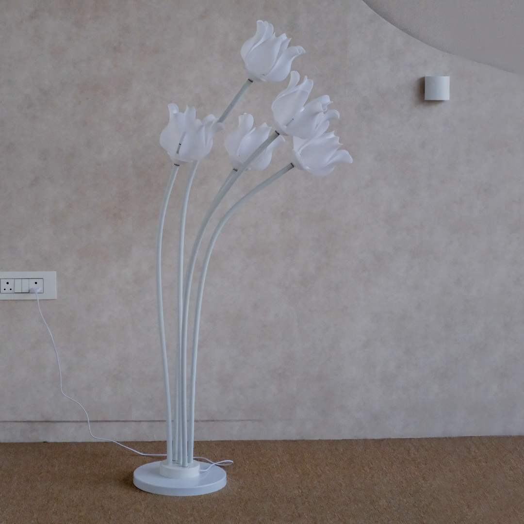 A modern white floor lamp with five curved stems and tulip-shaped flower heads, standing on a round base against a textured beige wall.