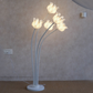 A modern floor lamp with five curved white stems ending in glowing white tulip-shaped flower shades, standing on a round white base against a textured beige wall.
