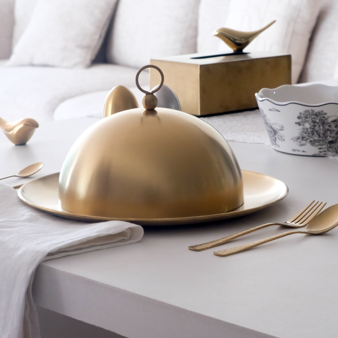 Gold dome-shaped serving dish on a table with silverware and a bowl in the background.