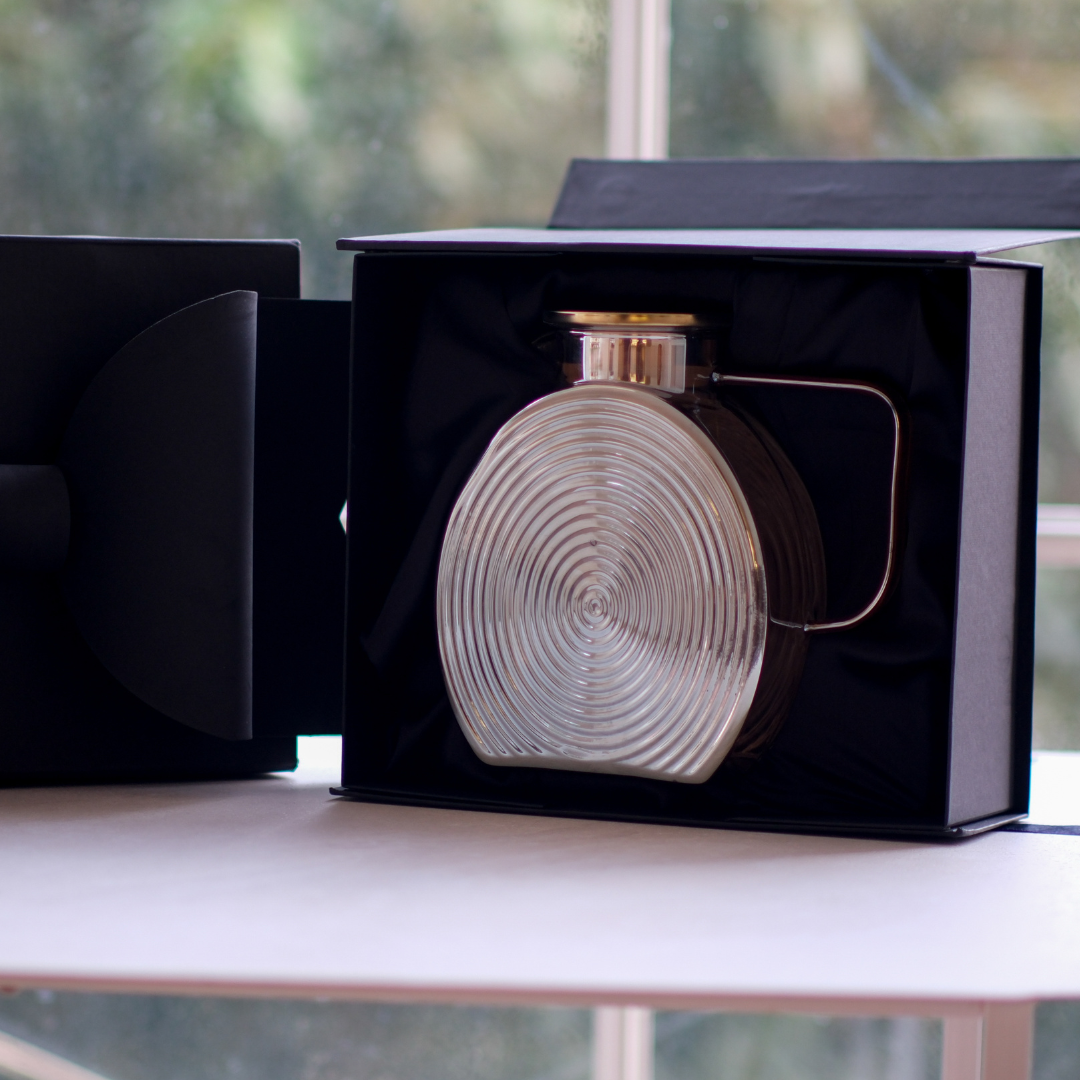 Brown glass jug with gold lid presented alongside premium black luxury gift packaging