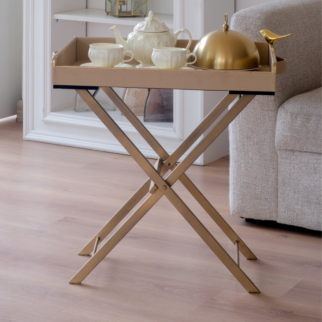 Elegant beige folding butler tray placed beside a sofa with a tea set, perfect for serving guests.