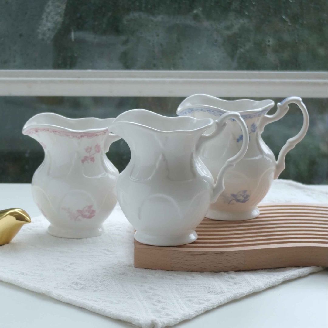 Premium ceramic milk creamer jugs in ivory, pink floral and blue floral finishes displayed for elegant tea, coffee and breakfast table settings.