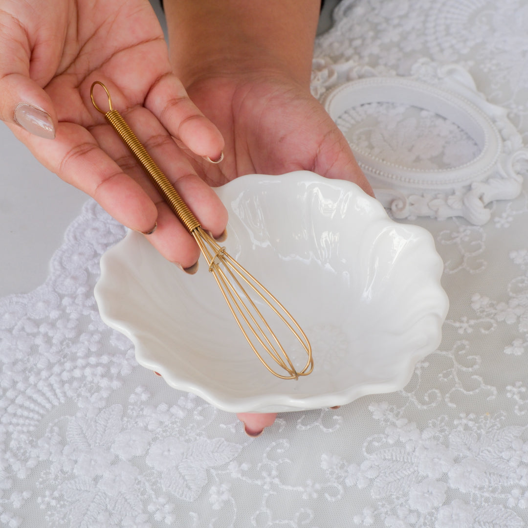 A lady holding a egg whisk over a bowl
