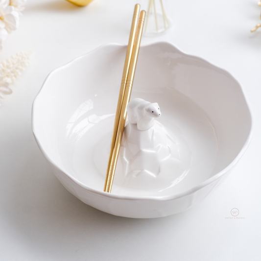Gold stainless steel chopsticks resting on a white ceramic polar bear bowl, luxury Asian dining tableware for noodles, ramen and sushi.