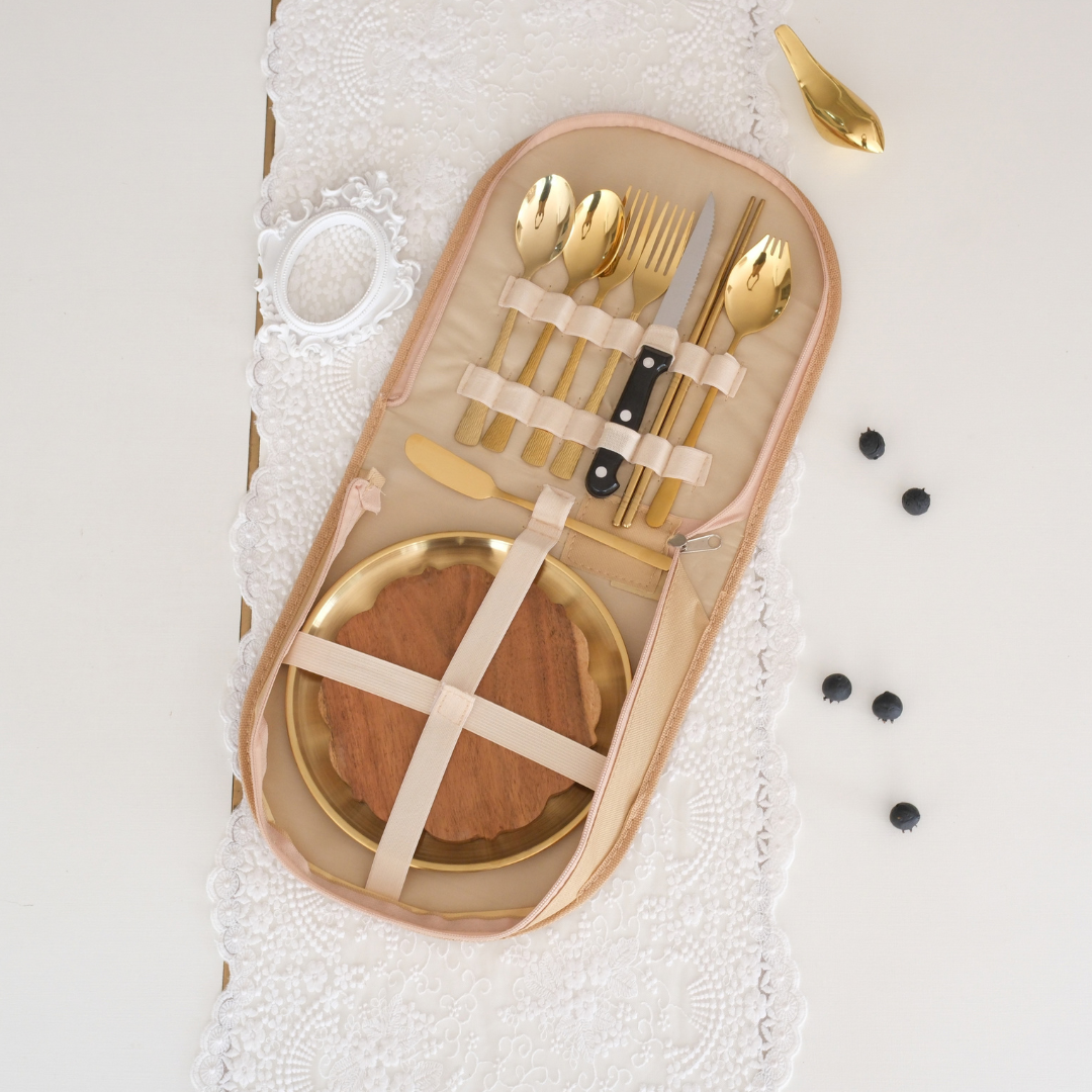Gold-plated cutlery and dinnerware set in a beige zippered organizer case with cream elastic bands