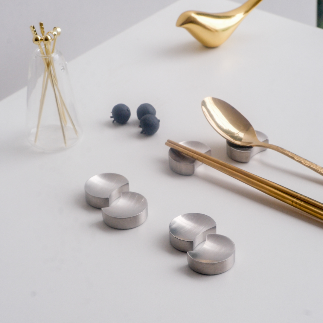 Silver chopstick holders and gold spoon on a white surface