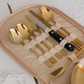 A gold-toned cutlery set with a knife featuring a black handle, organized in a beige zippered case with elastic loops. 