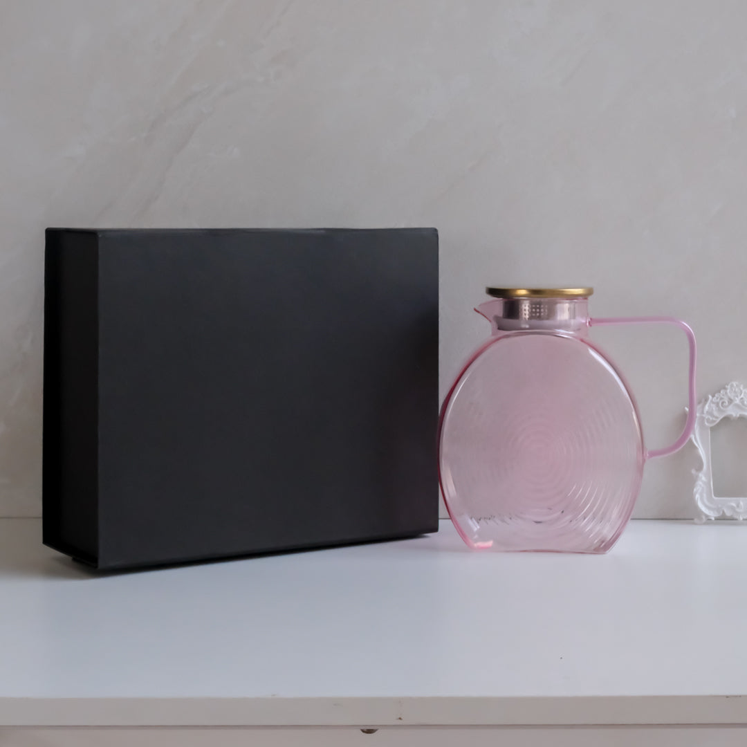 Pink glass jug with gold lid and handle, photographed with a luxury black gift box