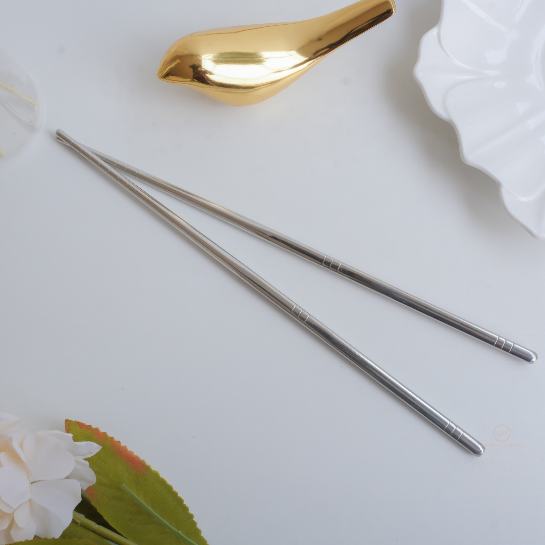 Elegant silver stainless steel chopsticks on a white tabletop with luxury dining accessories and ceramic tableware.