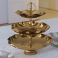 Three-tiered gold serving tray on a white surface with a blurred background