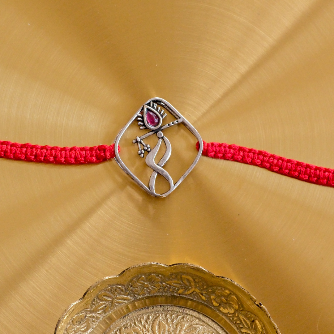 Close-up of a handcrafted Pure Silver Lord Krishna Rakhi with ruby stone detailing and adjustable red thread for brothers.