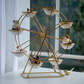 A gold metal Ferris wheel dessert stand with eight white ceramic bowls, displayed on a white table in front of a window.