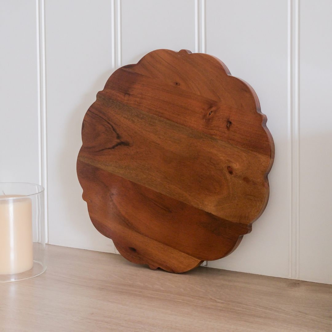 Round wooden serving board with rich natural wood grain and scalloped design.