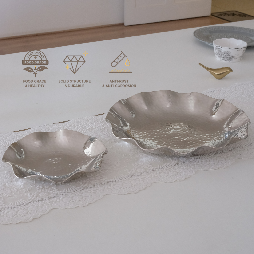 Two silver-toned scalloped ceramic or glass bowls placed on a white table runner, with printed feature icons along the top left and a small gold spoon in the background.
