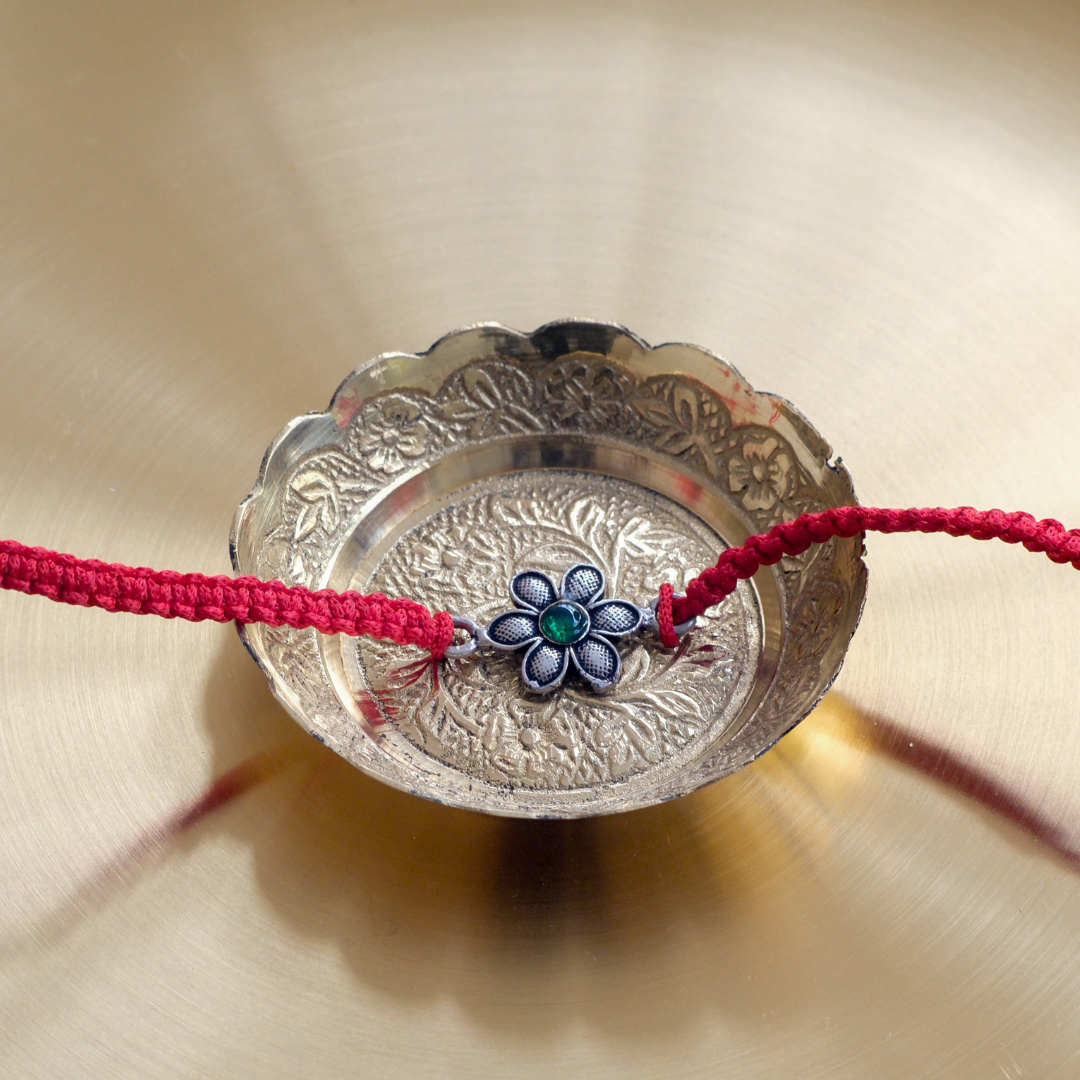 Pure silver floral rakhi featuring a pink gemstone centerpiece on a yellow and red braided thread, perfect for Raksha Bandhan gifting for brother.