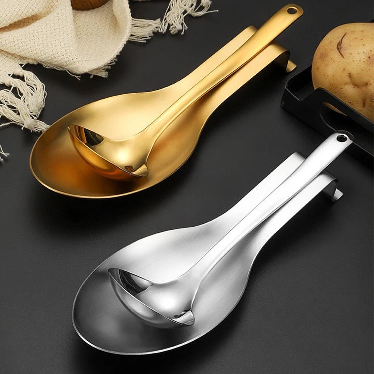 Two stainless steel spoon rests in gold and silver finishes, one displayed above the other, with a potato and a napkin in the background.