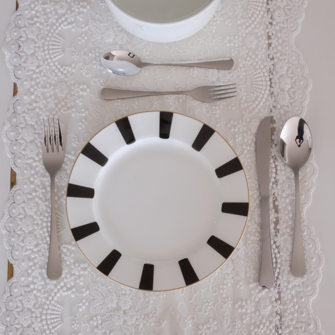 Stainless steel dinner cutlery set with spoon, fork and knife arranged on a decorative grey ceramic dinner plate