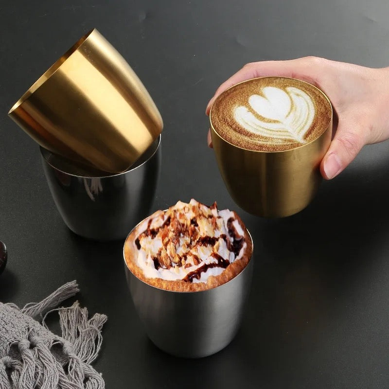 Two gold and black coffee cups with different types of coffee on a dark surface.