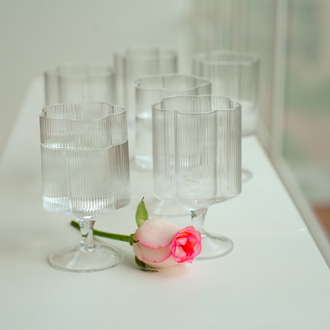 Set of clear glass goblets on a white surface with a pink flower.