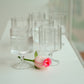 Set of clear glass goblets on a white surface with a pink flower.
