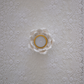 A white ceramic flower-shaped candle holder containing a tealight candle, set against a textured white lace background.