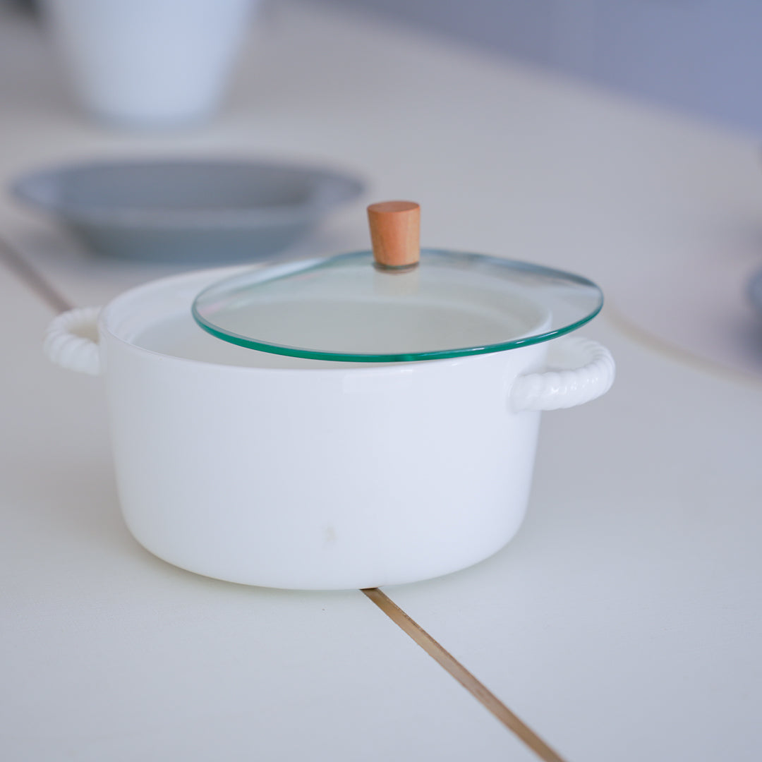 White ceramic casserole pot with glass lid and wooden knob on a tabletop