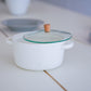 White ceramic casserole pot with glass lid and wooden knob on a tabletop