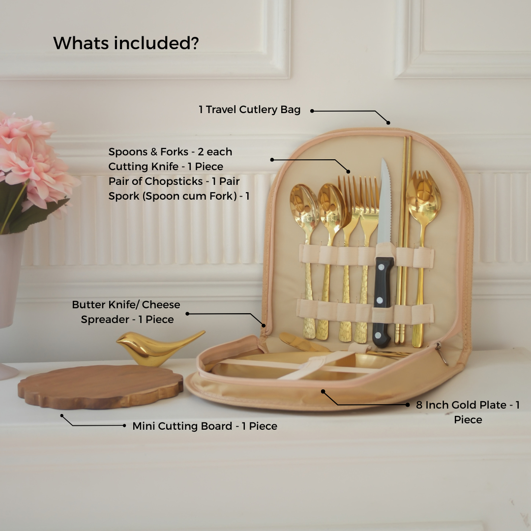 An open beige travel cutlery bag displayed on a white surface with overlaid text labels listing included utensils: two spoons, two forks, a cutting knife, a pair of chopsticks, a spork, a butter knife, a cheese spreader, and an 8-inch gold plate. A mini wooden cutting board and pink flowers are also shown in the scene.