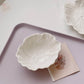 Two white porcelain dessert bowls with embossed flower patterns on a pink tray, one of the bowls contains a note card.
